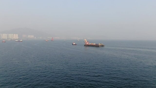 Barge loaded with Concrete mixer trucks pulled to port by a Tugboat in Hong Kong bay, Aerial view.