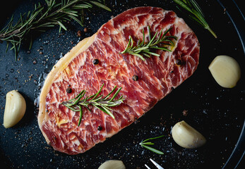 Raw fresh beef steak with olive oil, Colorful pepper, garlic and the rosemary leaf fresh on in the black tray on the wooden table, Top view.