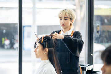 Asian professional female stylist cutting woman's hair in salon. The woman hairdresser using...