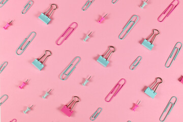 Stationery items like paper clips and drawing pins arranged on pink background