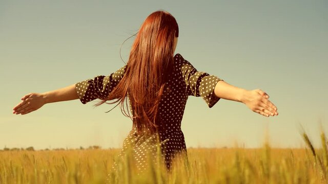 Happy young girl runs in slow motion across field, touching ears of wheat with her hand. Beautiful free woman enjoying nature in warm sunshine in wheat field on a sunset background. Girl travels.