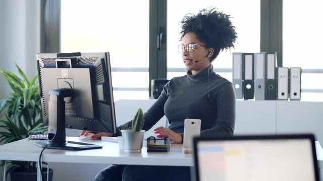 Video of beautiful young afro business woman working while making video call with computer sitting in the office.