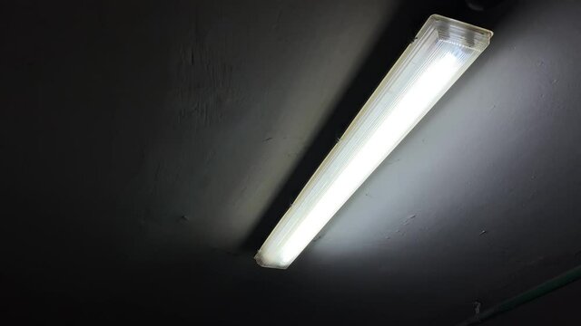 Broken flickering fluorescent lamp flashes on the ceiling of a dark room in underground parking lot