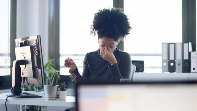 Video of exhausted young afro woman with headache working with computer in the office.