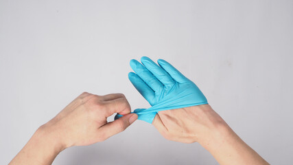 Left hand is pulling right hand with blue latex gloves on white background.