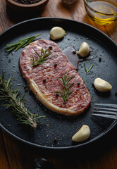 Raw fresh beef steak with olive oil, Colorful pepper, garlic and the rosemary leaf fresh on in the black tray on the wooden table, Top view.