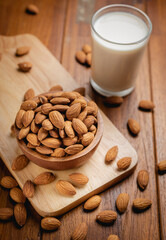 Almond milk in the glass with almond in the wooden bowl on the wooden table.