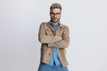 young casual man in beige jacket with glasses crossing arms