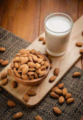 Almond milk in the glass with almond in the wooden bowl on the wooden table.