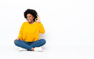 Young African American woman sitting on the floor showing ok sign with fingers