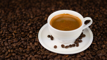 Coffee couple cup and saucer, the cup is filled with coffee, the saucer stands on a pile of roasted coffee beans