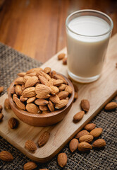 Almond milk in the glass with almond in the wooden bowl on the wooden table.