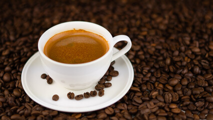 Side view, Coffee couple cup and saucer, coffee is poured in the cup, the saucer stands on a pile of roasted coffee beans
