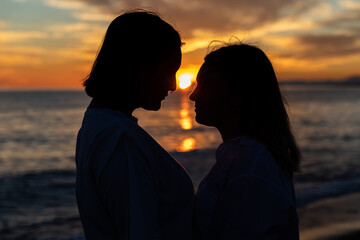 Joven pareja lesbiana mirándose bajo un atardecer a través de una silueta oscura con precioso mar...