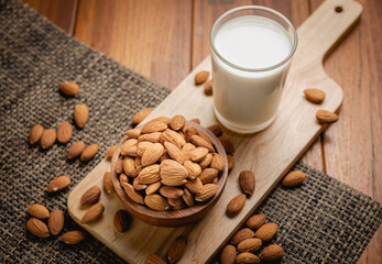 Almond milk in the glass with almond in the wooden bowl on the wooden table.