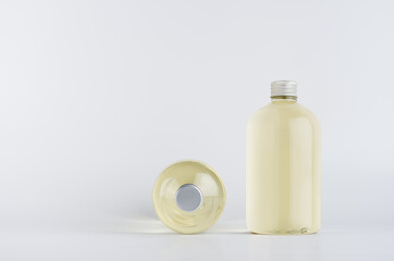 Set of two transparent plastic low thick bottles standing and lying with pale fresh drink or cosmetic essential oil and silver cap, mockup on white background,  front and top view.