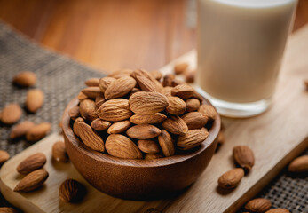 Almond milk in the glass with almond in the wooden bowl on the wooden table.
