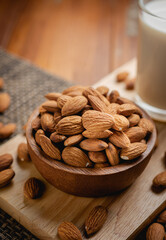 Almond milk in the glass with almond in the wooden bowl on the wooden table.