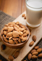 Almond milk in the glass with almond in the wooden bowl on the wooden table.