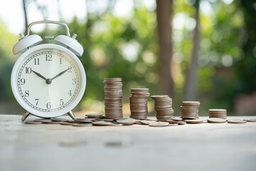 Alarm clock and a pile of golden coins on the table, Concept of opportunity cost time and Money saving.  Arrange coins into heaps with hands, content about money.