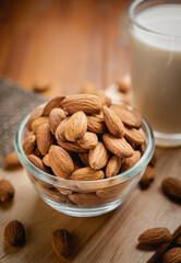 Almond milk in the glass with almond in the glass bowl on the wooden table.