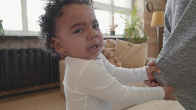 Handheld slowmo shot of fussy toddler boy tugging on mothers shirt and looking at camera
