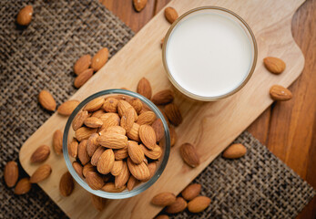 Almond milk in the glass with almond in the glass bowl on the wooden table.