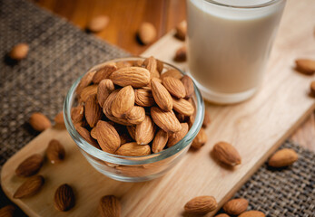 Almond milk in the glass with almond in the glass bowl on the wooden table.