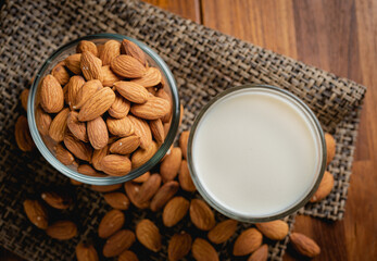 Almond milk in the glass with almond in the glass bowl on the wooden table.