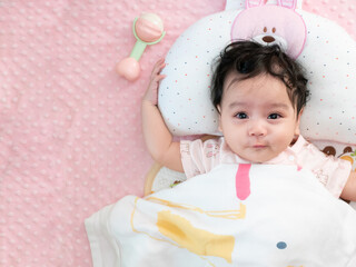 Top view of a cute little asian baby girl wrapped in a blanket lying on the bed, looking at camera