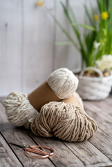 on a wooden background are two skewers of rope for macrame. Weaving macrame. Accessories in the form of a twine for weaving macrame and scissors with gold handles and a wooden stick lie on the table 