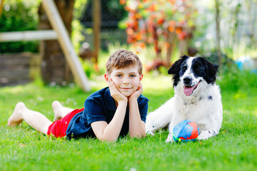 Active kid boy playing with family dog in garden. Laughing school child having fun with training dog, running and playing with ball. Happy family outdoors. Friendship between animal and kids
