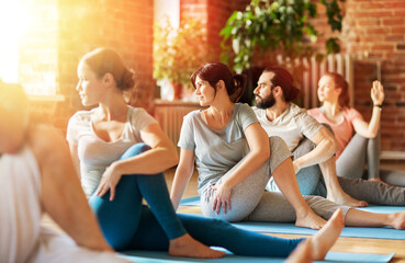 fitness, sport and healthy lifestyle concept - group of people doing yoga seated spinal twist pose in gym or studio