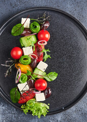 Fresh greek salad with tomato, cucumber, bel pepper , olives and feta cheese on black plate,...