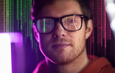 virtual reality, technology and programming concept - portrait of smiling young man in glasses over ultra violet neon lights and binary code on dark background