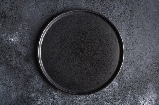 Empty round black plate on dark moody dark background with copy space. Overhead view