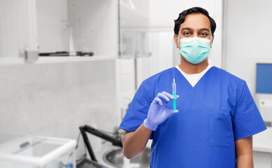 Fototapeta na wymiar healthcare, vaccination and medicine concept - indian doctor or male nurse in blue uniform, face mask for protection from virus disease and gloves with syringe over laboratory or hospital background