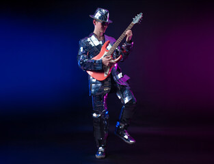 Fototapeta na wymiar a male artist in a mirrored suit and hat with an electric guitar on a dark background
