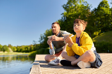 family, generation and food concept - father and son with tablet pc computer eating sandwiches on river berth