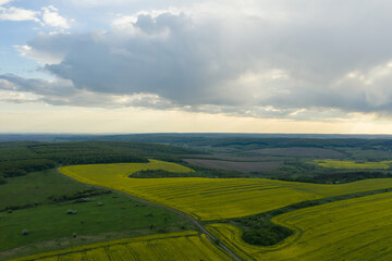 Obraz premium Splendid panoramic view of agriculture fields in countryside and cloudy sky on a spring day. Ukrainian landscapes. Yellow harvest fields and green forests. Green wheat fields. Drone shot.