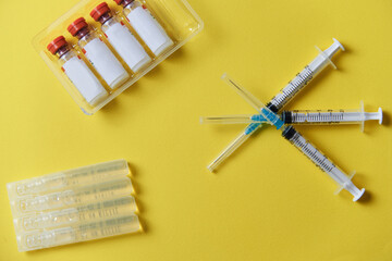 three syringes, a medical dressing, and vials for injecting the vaccine on a yellow background. 