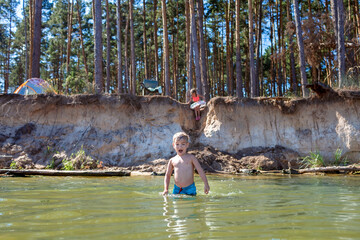 Kids swimming in the forest lake near campsite during family local travel, camping tent, fireplace, fresh air and healthy lifestyle. Sustainable green tourism and vacation. Stay and explore local