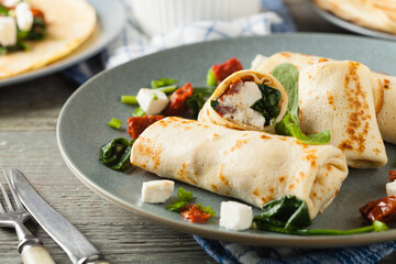 Pancakes with spinach, feta and dried tomatoes. Served on a gray plate. Wooden natural background.