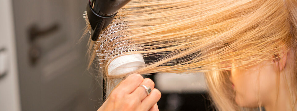 Close up of hairdresser's hand is drying hair of the blonde young woman in a hair salon