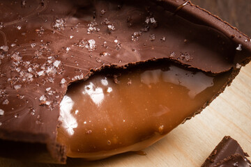 Close up of a cracked chocolate easter egg with flower of salt, stuffed with dulce de leche (dripping) on a wooden stand on a wooden table.
