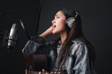 Obraz na płótnie Canvas Asian female singer with a passion for music and microphone. While playing her guitar in a professional studio. Music concept, sound recording concept.