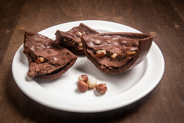 Cracked stuffed chocolate and hazelnut easter egg on a white plate on a wooden table.