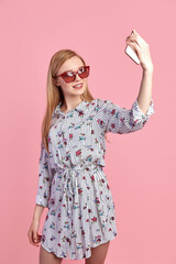 Young girl in sunglasses wearing floral dress, straw hat, isolated over pink background.