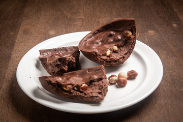 Cracked stuffed chocolate and hazelnut easter egg on a white plate on a wooden table.
