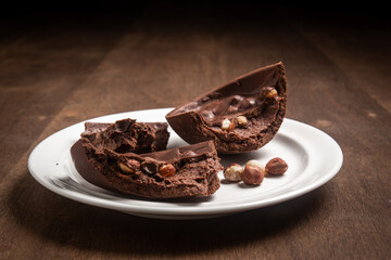 Cracked stuffed chocolate and hazelnut easter egg on a white plate on a wooden table.
